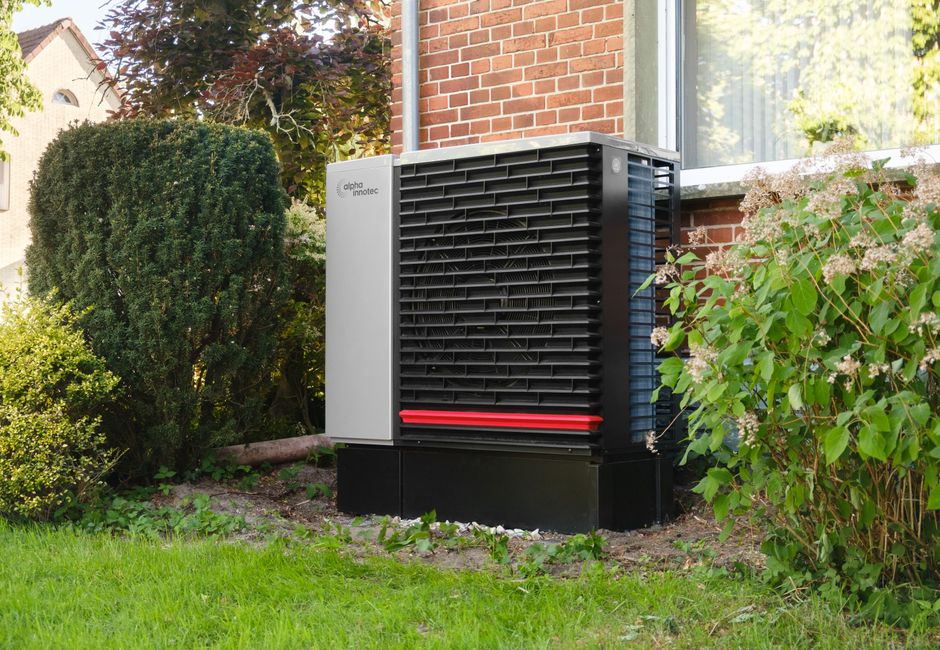 Unité extérieure de pompe à chaleur air/air posée dans le jardin verdoyant d'une maison