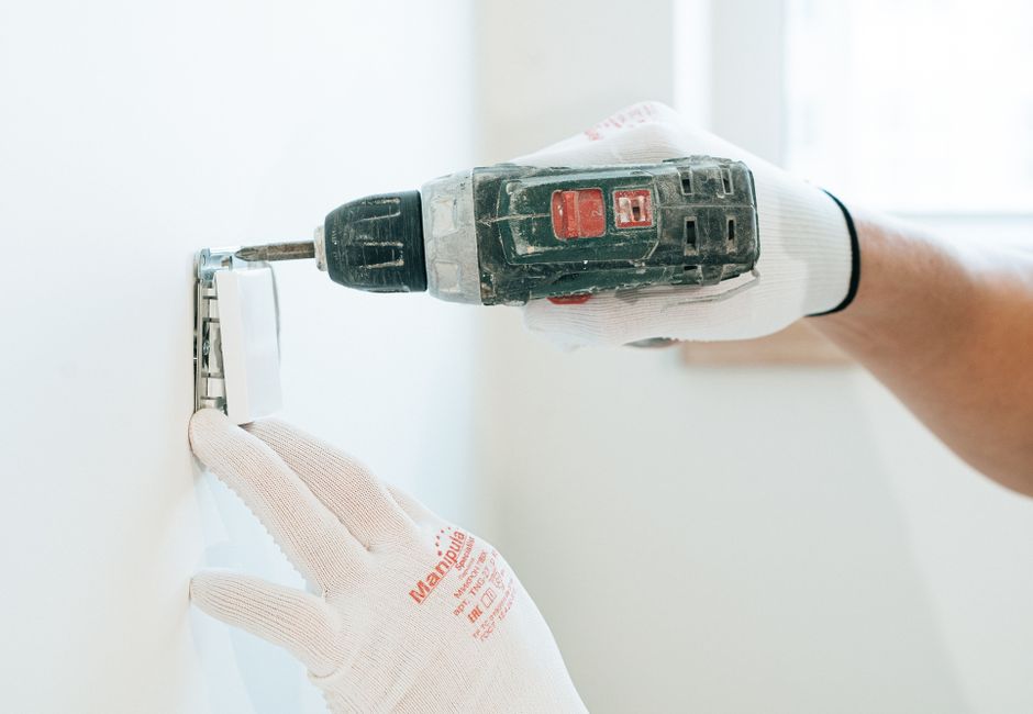 Installateur fixant à la perceuse le support mural d'une climatisation, gants de protection